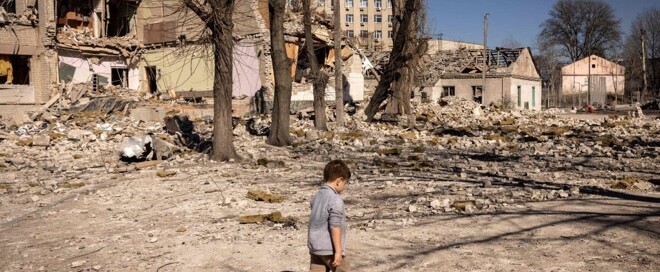 A child walks in front of a damaged school in the city of Zhytomyr, in northern Ukraine (March 23, 2022)
